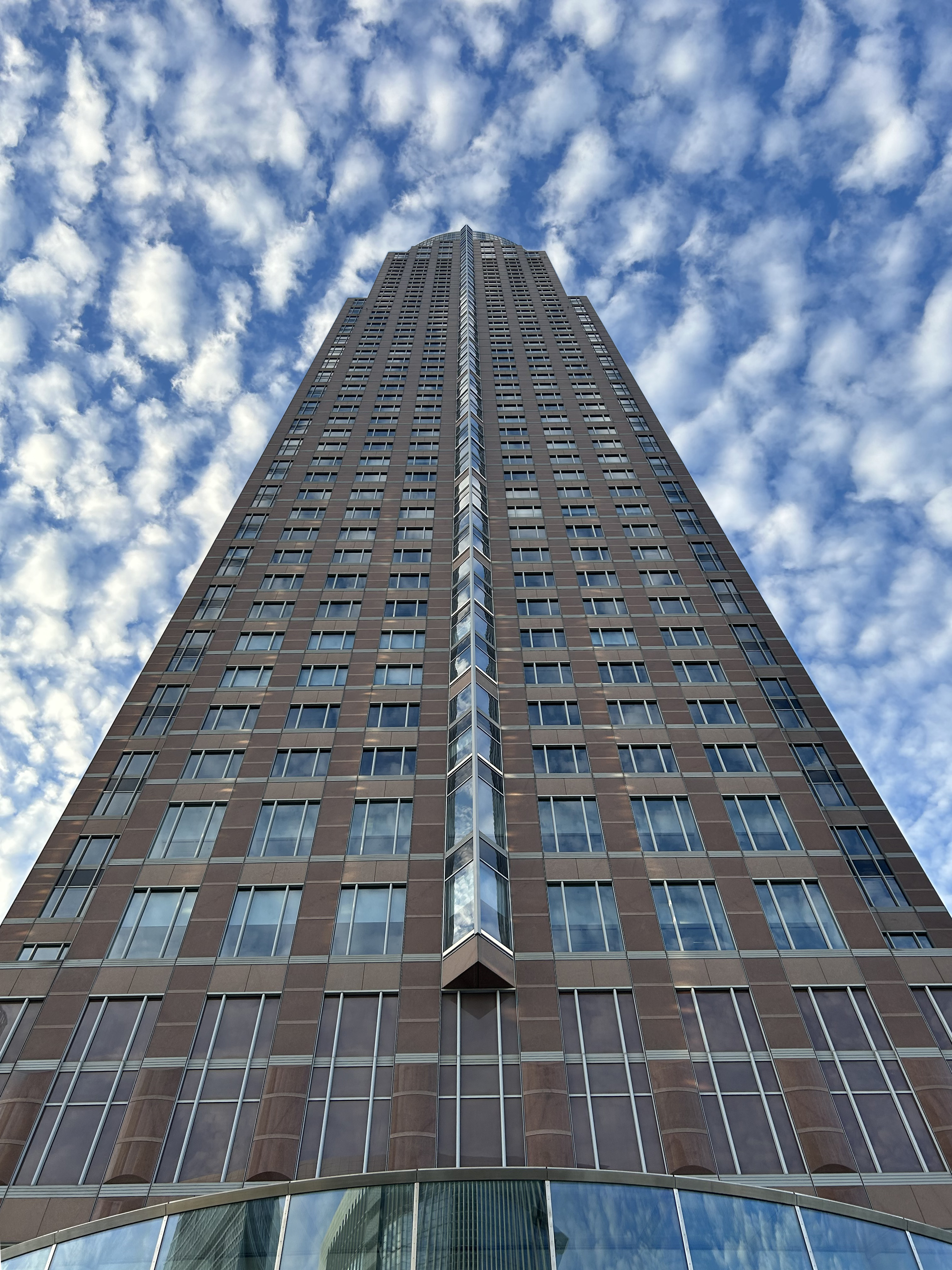 Der Frankfurter MesseTurm ragt vor einem wolkigen, blauen Himmel empor.